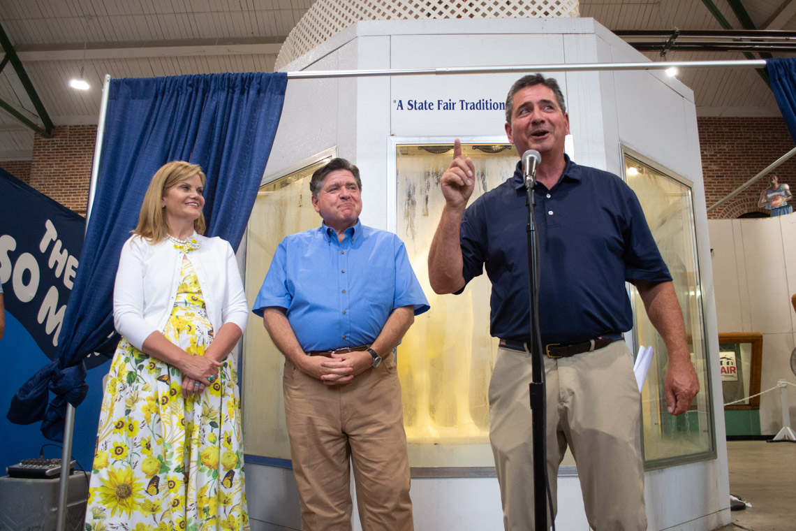 Jerry Costello speaks into a microphone as JB and MK Pritzker watch.