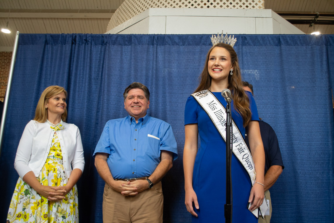 Krista Phillips stands in behind a microphone in front of JB Pritzker and MK Pritzker.